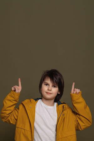 Your promo here. Portrait of attractive little boy in casual clothes pointing fingers up at...