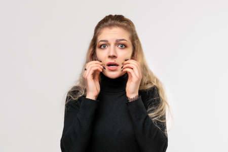 Close up blonde girl looking worried, anxious, stressed and afraid, hold hands near mouth. True...