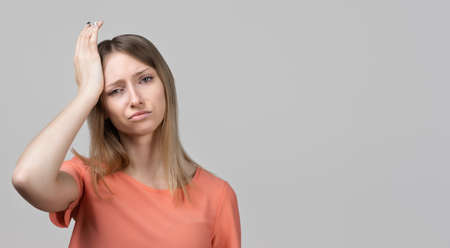 Concerned, frustrated young blond girl feeling fatigue, as suffer pain in head, painful headache or migraine. Studio shot, gray background. Place for adの写真素材