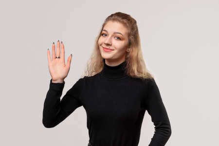 Close up friendly blonde girl is saying hello, saluting with hand with happy expression, showing five fingers, friendly welcome gestureの写真素材