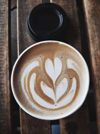 A cup of hot latte, cappuccino or espresso coffee with milk foam on a rustic table, view from top. Milk foam in shape leaf tree on top of latte art from professional barista artistの写真素材