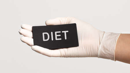 Closeup of the hand in a white sterile glove holding a card with word - Diet. Medical conceptの写真素材