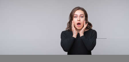 Portrait of shocked afraid woman looking with having wide open mouth gesturing palms, standing gray...