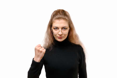 Aggressive young woman wearing casual black clothes shaking fist and looking at camera, standing...