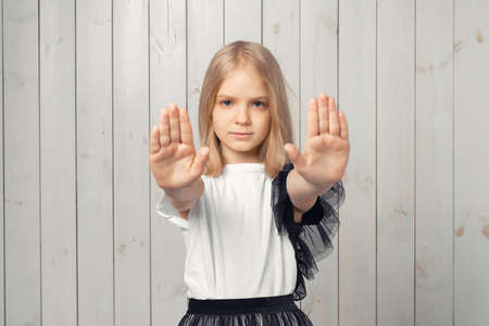 I say no. Serious blonde teen girl keeps both palms forward at camera, makes forbid sign, restricts or warns, extends arm in stop sign. Studio shot, light wooden backgroundの写真素材