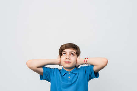 Portrait of young upset boy 12-14 years covering ears, asking for silence and looking up. Child on gray background. Copy space for your textの写真素材