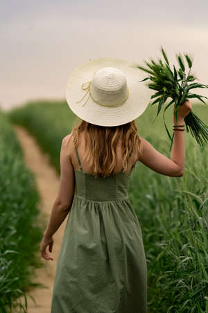 Young woman in a hat walking in a wheat field, enjoys life and summer. Wheat field. Beautiful Nature Landscape under Sunlight. Healthy lifestyle Concept. Image with noise, film grainの写真素材