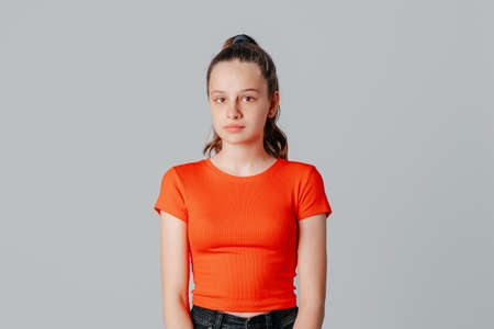 Beautiful brunette teen girl with clean glowing facial skin, looking at camera, standing over gray backgroundの写真素材