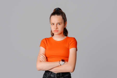 Angry brunette teen girl feel unfair and displeased, cross arms on chest and frowning, condemn...