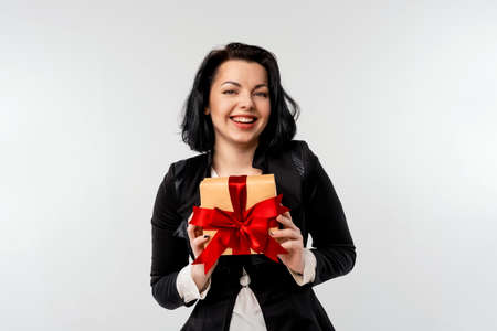 Young businesswoman hold gift, wearing black formal suit jacket. Smiling happy girl on white backgroundの写真素材
