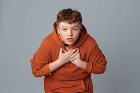 Who me. Are you talking about me. Handsome plus size teenager boy pointing hands at himself, standing over gray background, having doubtful confused uncertain facial expressionの写真素材