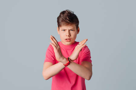 Stop. Serious teenager boy in casual pink t shirt, with crossed arms showing stop sign, standing over gray backgroundの写真素材
