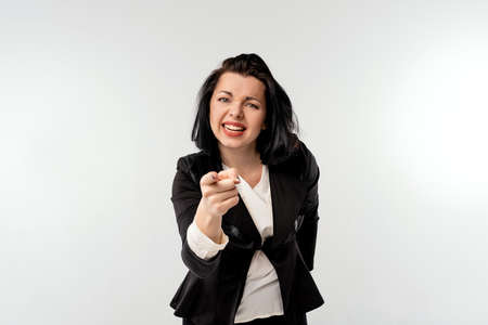 Businesswoman in black formal jacket white shirt pointing at camera with an angry aggressive expression looking like a furious, crazy boss, white background. Business conceptの写真素材