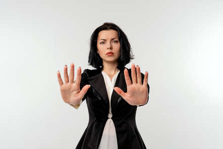 Serious young businesswoman in black formal jacket white shirt showing stop gesture with palms isolated on black background. Social distancing. New normal behavior. Business conceptの写真素材