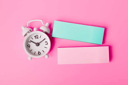 Still life, business, office supplies or education concept: colorful sticky notes and white alarm clock on the pink background. Top view, space for your textの写真素材