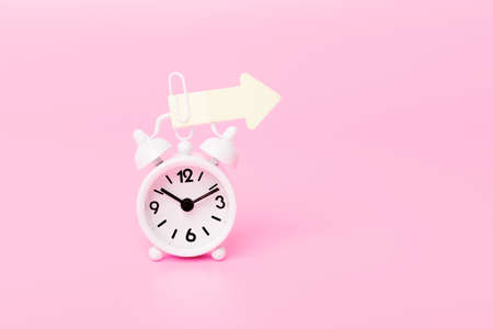 white alarm clock and colorful arrow pointing to the right on pink background, direction arrow....