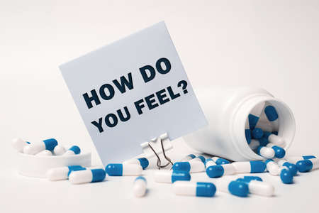 Text - How Do You Feel, written on sticky note near blue-white pills spilling out of pill bottle. medical conceptの写真素材