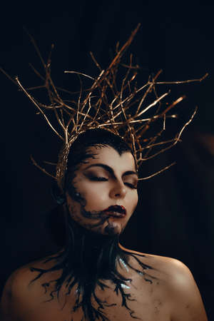 Fantasy portrait of emotional gothic woman dark witch. Girl goddess in in golden crown from branches. Beautiful face black art makeup. Art photo, black backgroundの写真素材
