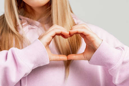 Cropped view blonde girl making a heart symbol with her hands. Female hands showing a heart shape. Sign of love, harmony, gratitude, charity. Feelings and emotions conceptの写真素材