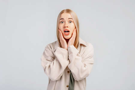 Amazed blond girl looking worried and shocked, hear breaking news, wears casual clothes, stands...