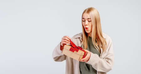 Excited young woman opening present gift box. Pretty girl smiling and posing with gift box on light...
