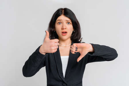 Weighing decision. Indecisive brunette teen girl in black blazer makes choice, shows thumb up and...