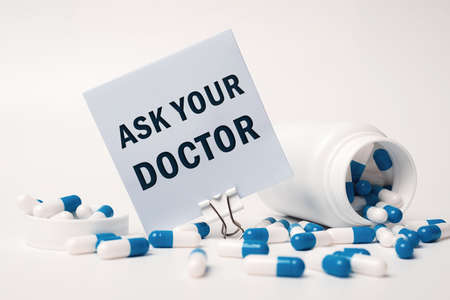 ASK YOUR DOCTOR, inscription on paper note near blue-white pills spilling out of pill bottle. medical conceptの写真素材