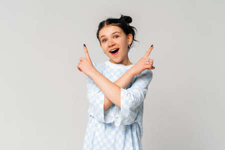 Portrait of indecisive dark-haired teen girl points sideways and smiles, concept of choice,...