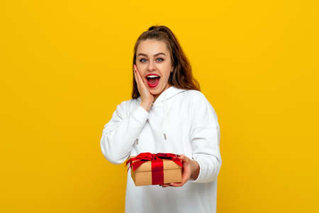 Happy pretty girl with long chestnut hair smiling and showing gift box at camera, standing on yellow background. Young woman in love, Receiving gifts from friends. holiday conceptの写真素材
