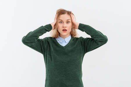 Shocked concerned young blonde woman 20s, wearing casual clothes, holds hands on on her head, look worried as facing difficulties. Indoor studio shot on white backgroundの写真素材