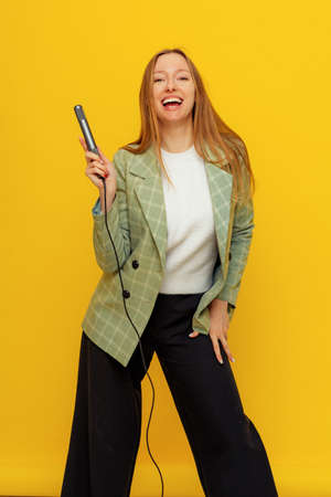 Vertical shot of joyful pretty woman singing a song with a microphone, presenting an event or having...