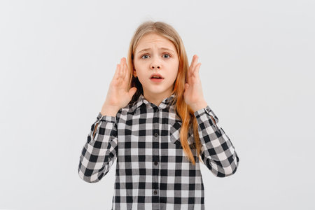 Portrait of girl with blonde hair looking shocked and concerned at camera, open mouth and furrow eyebrows startled, hear awful terrible news, stands in casual plaid shirt over white studio backgroundの写真素材