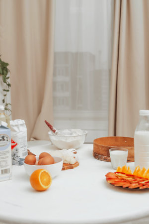Image of domestic kitchen with white table and fruits on it. Eggs, flour and milk on wooden white table. Baking background with cake ingredients. Healthy light meals for breakfastの写真素材