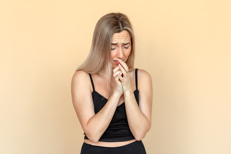 Fright. Portrait of the scared young woman with freckles and close eyes. Worried girl wearing casual black clothes standing over beige background. panic conceptの写真素材