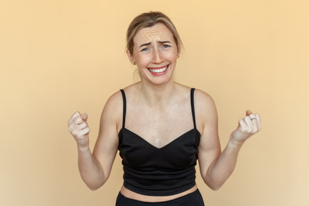 stress at work. Portrait of dissatisfied young woman gesturing hands. Sad girl wearing casual black clothes standing over beige background. Psychology, depression, bad mood, stressの写真素材
