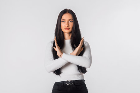 Portrait of brunette young woman hold hands crossed angry mood, standing over white studio background. Serious student girl refusing somethingの写真素材