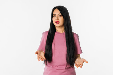 What's wrong. Confused beautiful woman spreads hands sideways, smirks face, feels doubt while makes choice, stand with confused look against white studio backgroundの写真素材