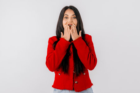 Portrait of girl looking shocked after hearing something, touches her mouth and looks speechless,...