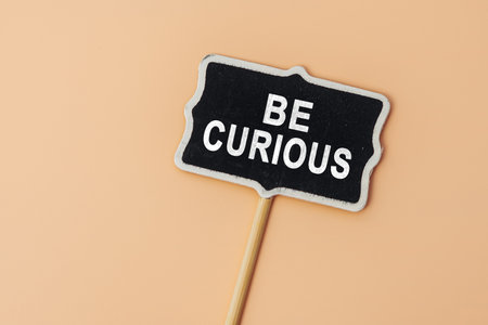 Be Curious - text on a small chalkboard on a beige background. top view. Communication and brainstormingの写真素材
