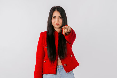 Its you. Lovely girl with long hair, points finger at camera and looks confident, standing over white background. Young leader woman wearing stylish red blazer points index finger on youの写真素材