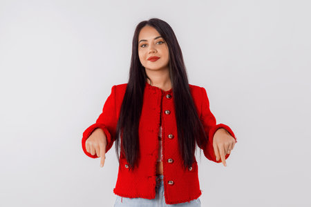 Lovely stylish young woman pointing fingers down, showing advertising, promo text, amazing news, offer. Studio shot, white backgroundの写真素材