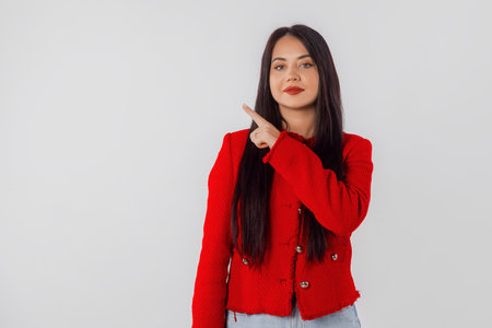 Lovely smiling young woman pointing fingers left, showing advertisement, amazing news, promo banner, offer. Studio shot, white background with copyspaceの写真素材