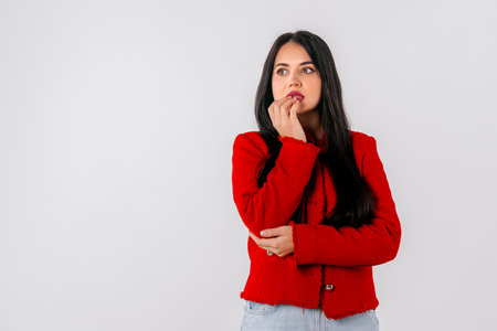 Anxious young woman bites fingernails, looks nervous, scared of smth, stands over white background. Amazed horrified female keeps hand on mouthの写真素材