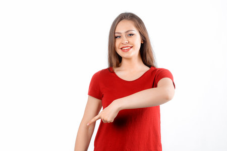 Smiling lovely girl points finger down, shows advertisement on blank white space. Young brunette female looking happy by promotion offer, stands over white backgroundの写真素材