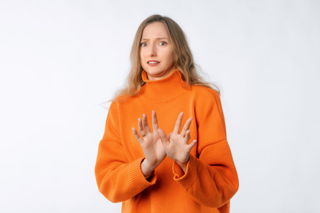 Portrait of young woman deny something, shakes hands and say no, rejects offer, looks insulted, express disapproval, wearing soft orange sweater, standing over neutral backgroundの写真素材