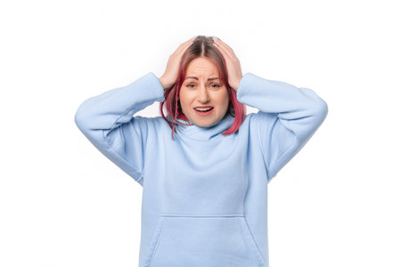 nervous woman with pink hair wearing blue hoodie standing over white background surprised with hand on head for mistake, remember error. Forgot, bad memory conceptの写真素材
