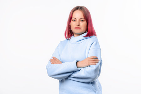 Portrait of confident young woman with arms folded, looks happy. Lovely female model with pink hair in a blue hoodie standing over white backgroundの写真素材