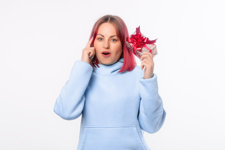 Happy young woman with pink hair wears blue hoodie hold shake present box with gift ribbon bow try to guess what inside, standing over white backgroundの写真素材