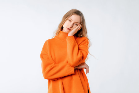 Bored woman thinking, looking complicated, dreaming of something, standing in soft orange sweater over neutral studio backgroundの写真素材