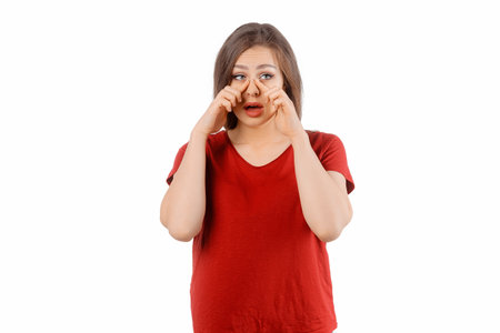Beautiful brunette woman rubs tired eyes. Winsome female model in red t shirt posing over white studio backgroundの写真素材
